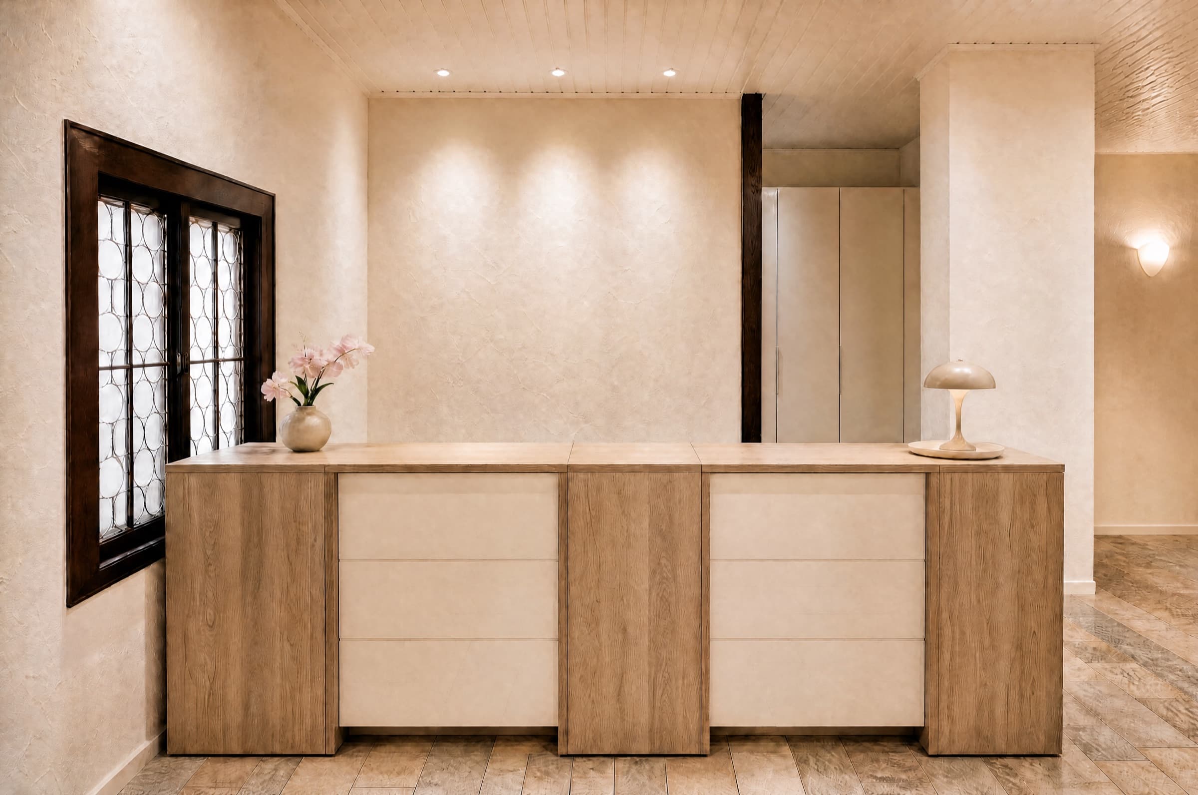 Empfangstresen aus hellem Holz mit weißen Fronten, daneben ein dunkel gerahmtes Bleiglasfenster