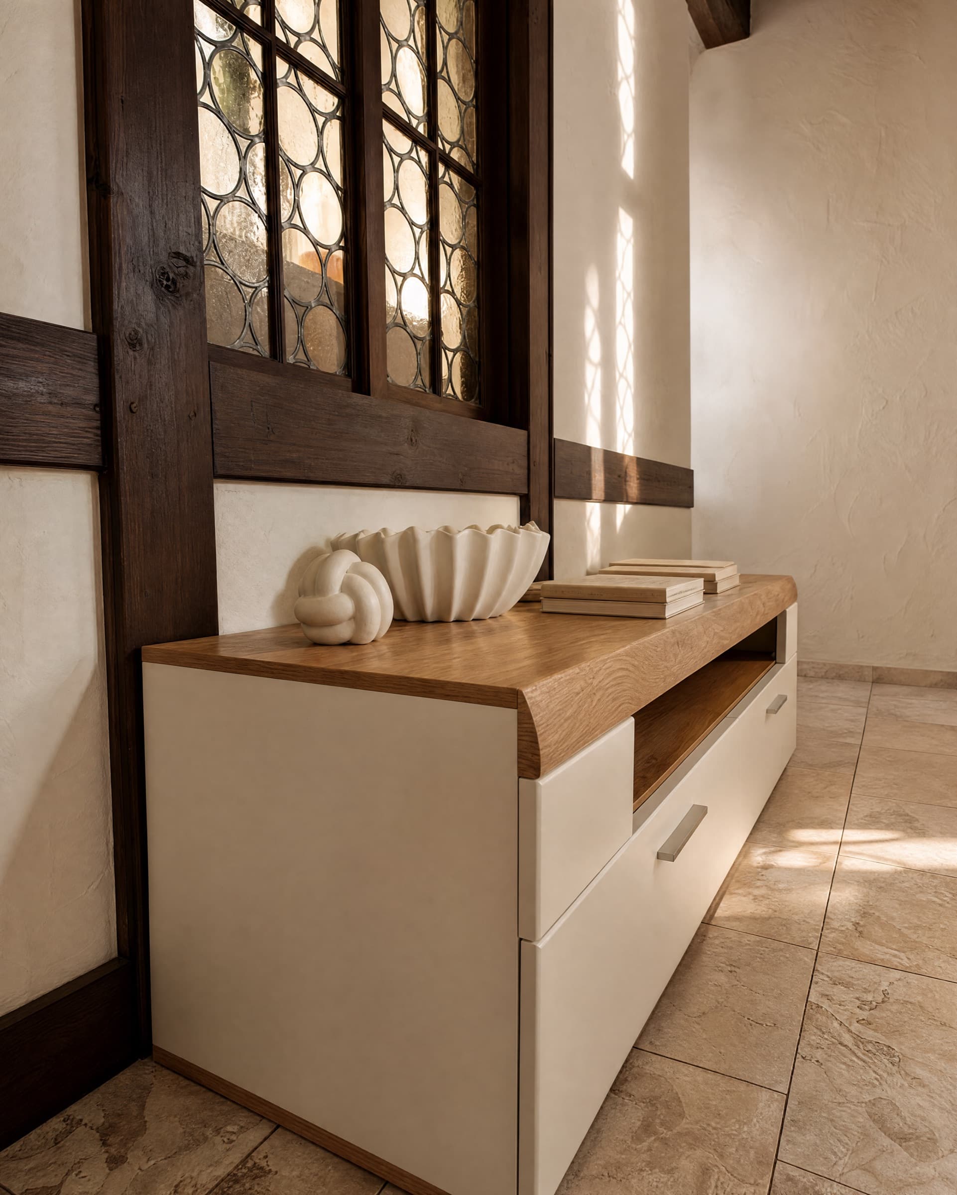 Altes Fachwerkfenster mit Butzenscheiben über einer hellen Kommode mit Eichenplatte, Lichtmuster an der Wand