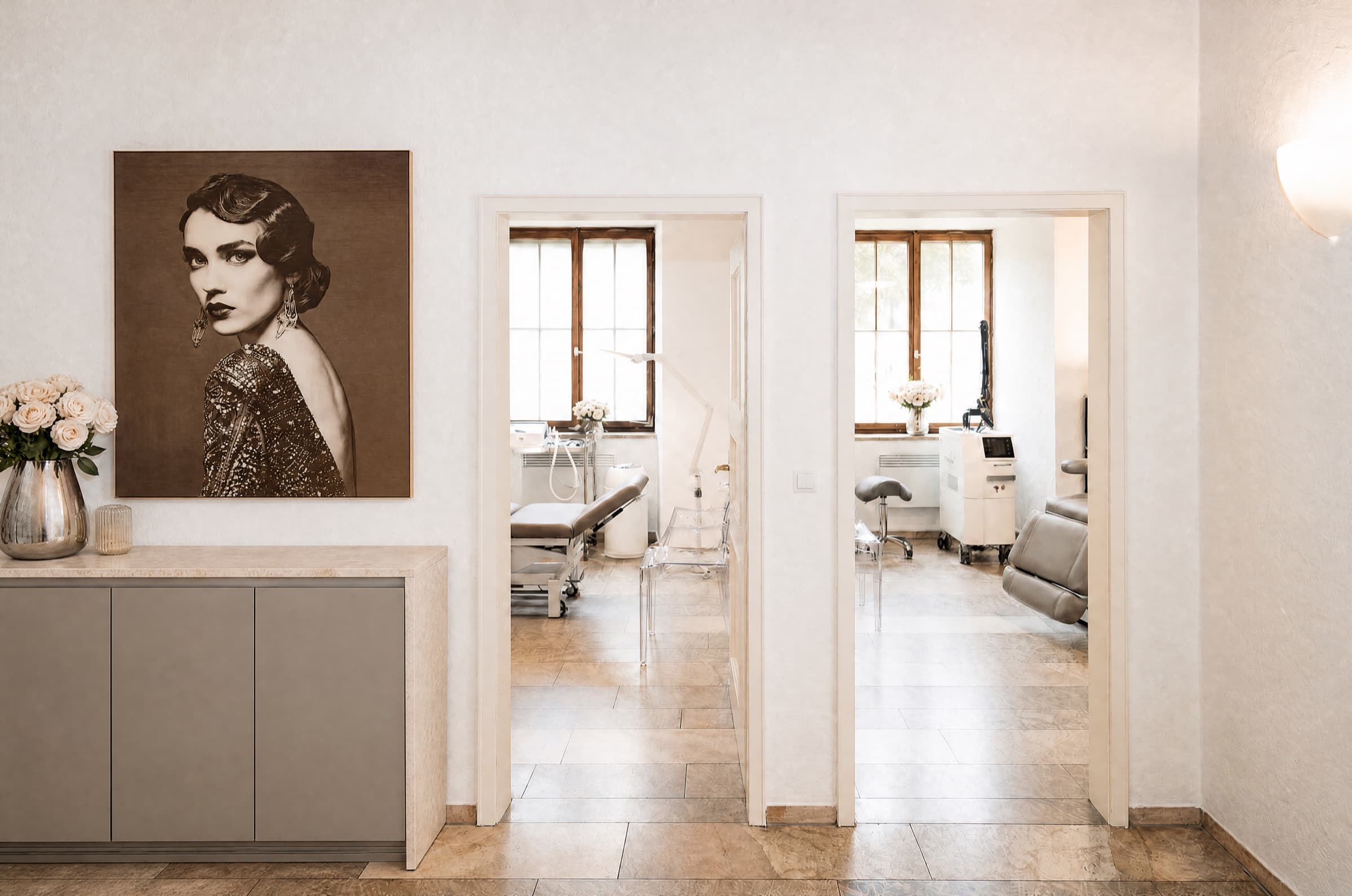 Flur der Praxis mit Steinplatten-Kommode und einem Art-déco-Porträt, daneben zwei offene Türen in die hellen Behandlungsräume