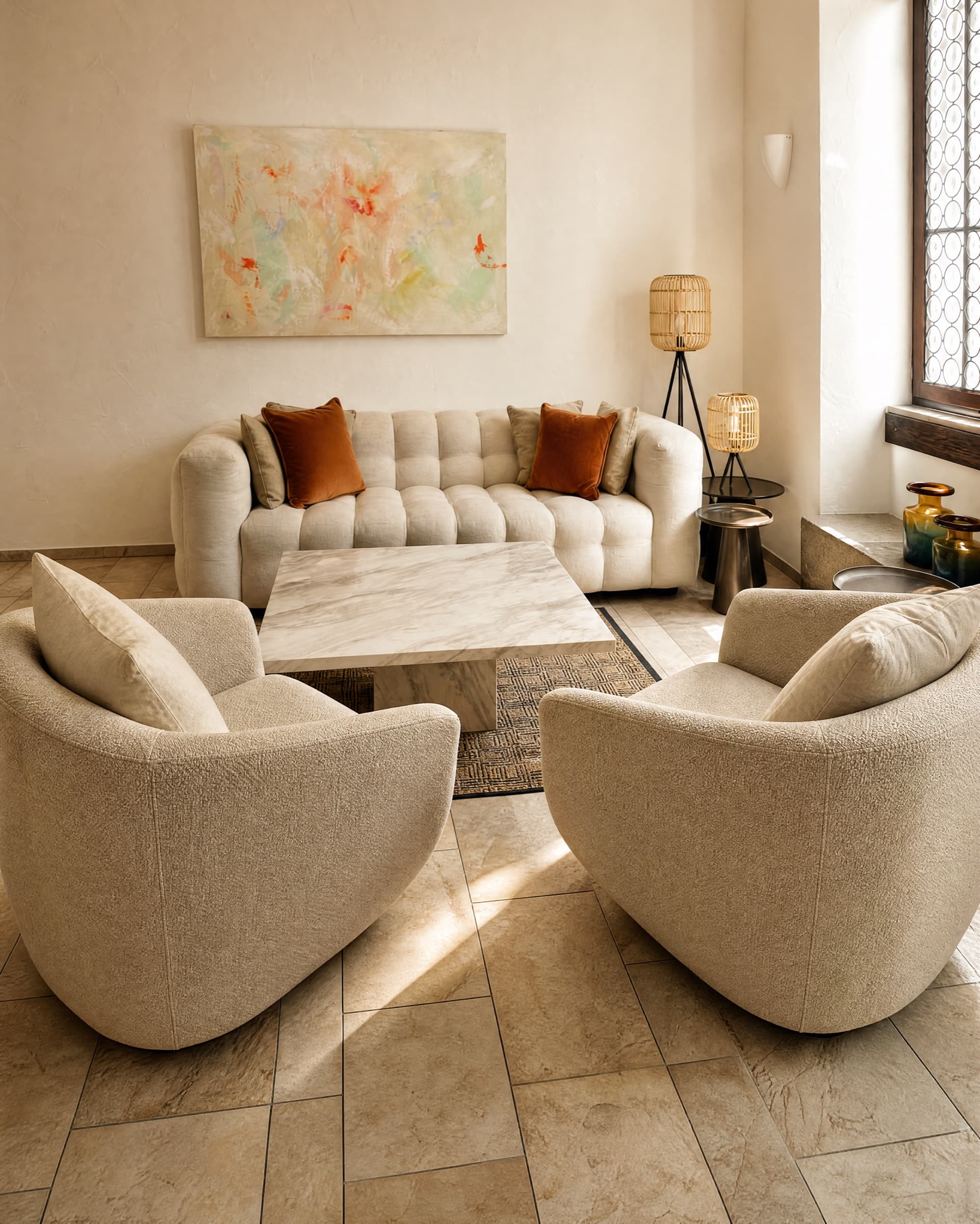 Zwei runde Sessel aus hellem Bouclé am Marmortisch im Wartezimmer, dahinter das Sofa mit rostroten Kissen